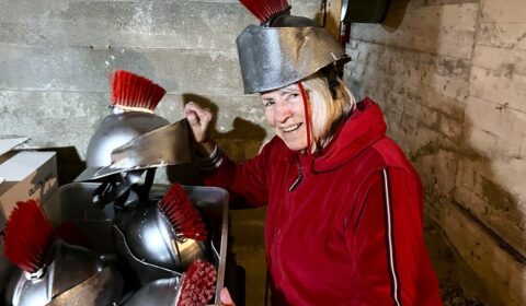 Glady Bryce tries on a centurian's helmet while getting out costumes stored under community centre.